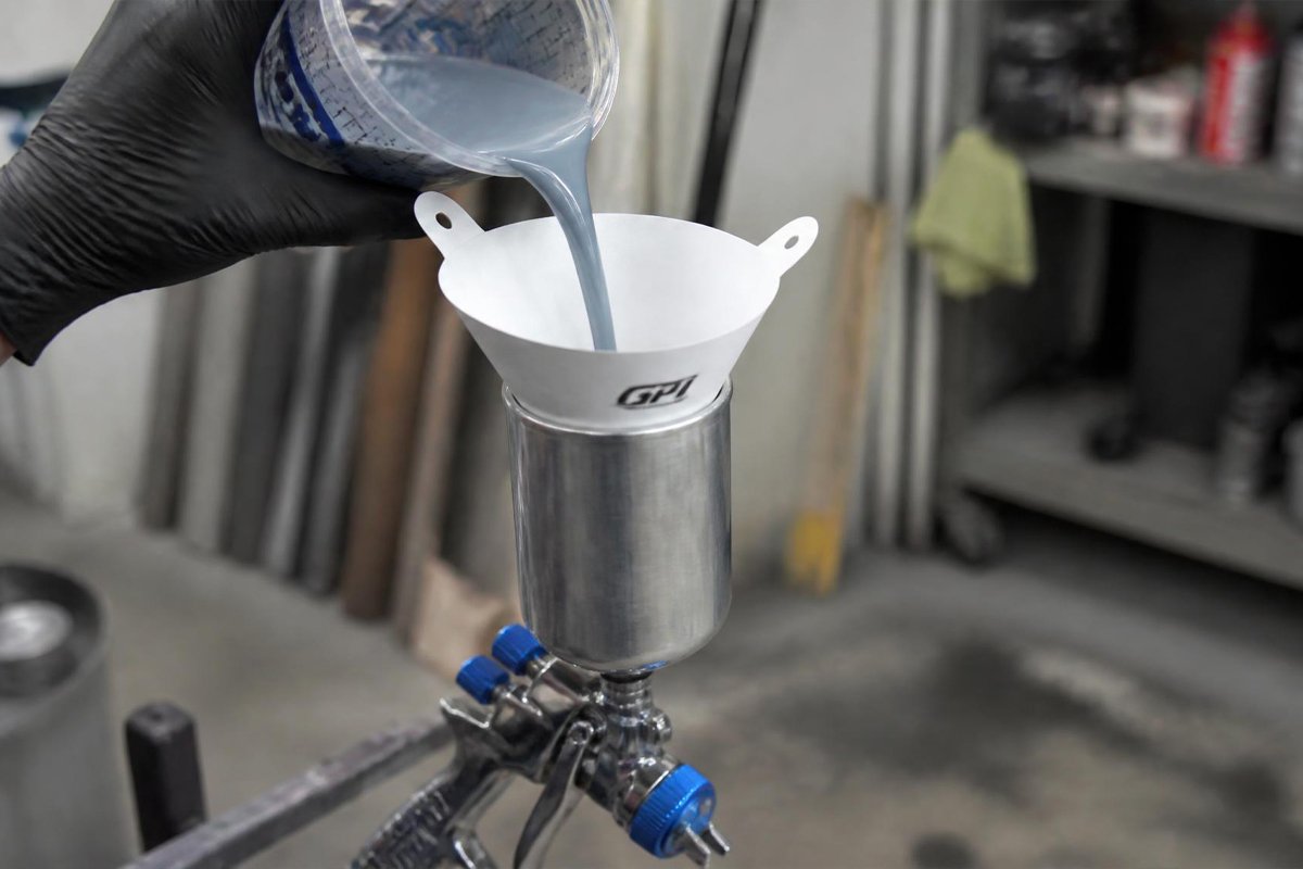 pouring paint through a cone strainer into a spray gun cup